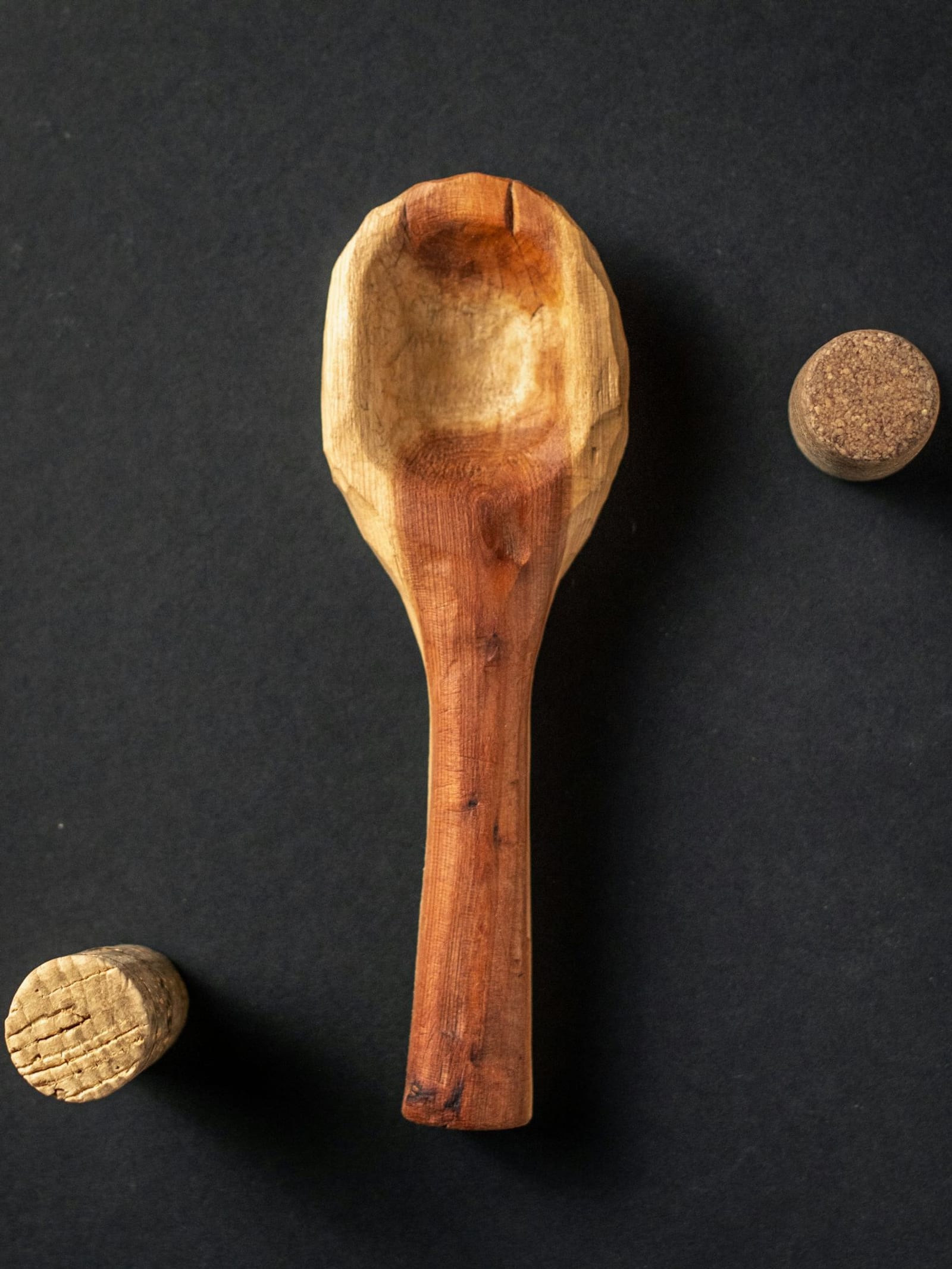 Una cuchara de madera tallada a mano sobre un fondo oscuro, junto a dos tarugos de madera.